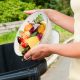 Unrecognizable woman emptying a collander of fruit and vegetable waste into a black plastic bin.
